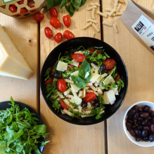 Photo d'une salade de pâtes de fusili, roquette, tomates cerises, tomates séchées, parmesan et olives noires